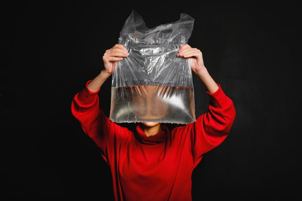 Person in Red Long Sleeve Top Holding Black Plastic Bag with Water Inside